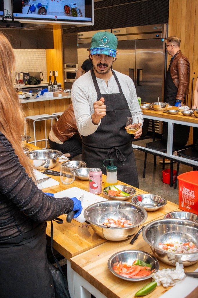 A chef teaching while a guest chops ingredients