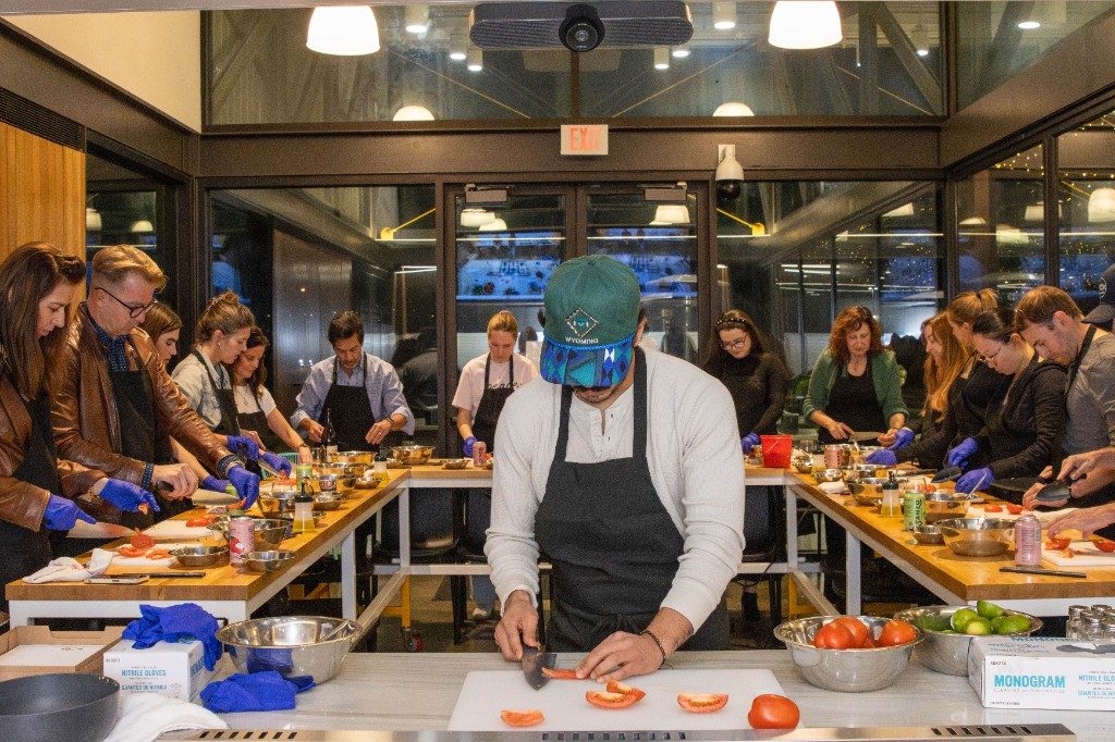 A full cooking class gathered around wooden prep tables